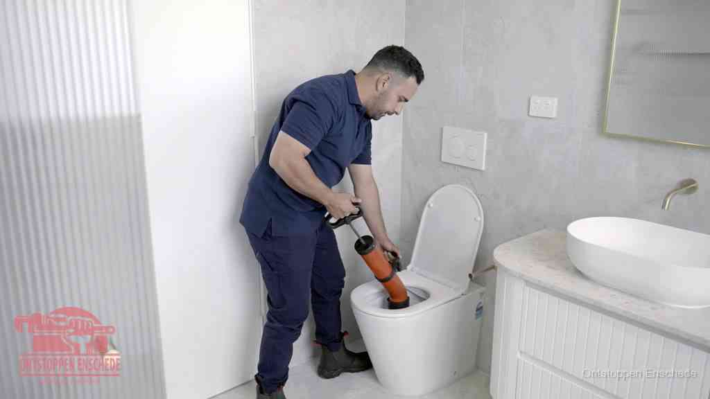 Een monteur buigt over een wandcloset en duwt met de hand een persluchtontstopper in de toiletpot om de verstopping handmatig los te maken in Enschede