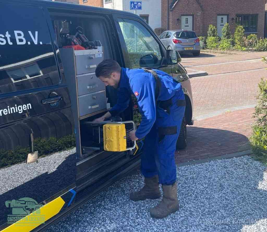 Een monteur pakt buiten op de oprit gereedschap uit de bedrijfsbus, het moment om een professional in te schakelen voor een verstopte afvoer in Enschede