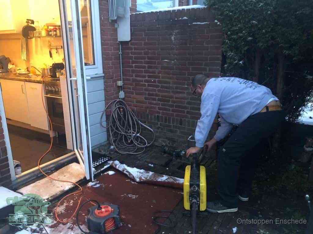 Een monteur werkt buiten bij een open riool-/grondput met een elektrische ontstoppingsmachine om een verborgen afvoerprobleem op te sporen in Enschede