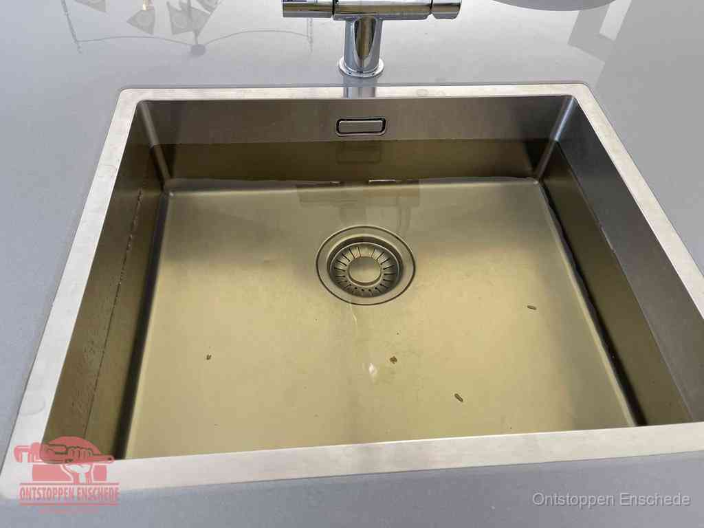 Stilstaand water in een rvs spoelbak dat niet wegloopt, een duidelijk signaal van een gootsteenverstopping in Enschede