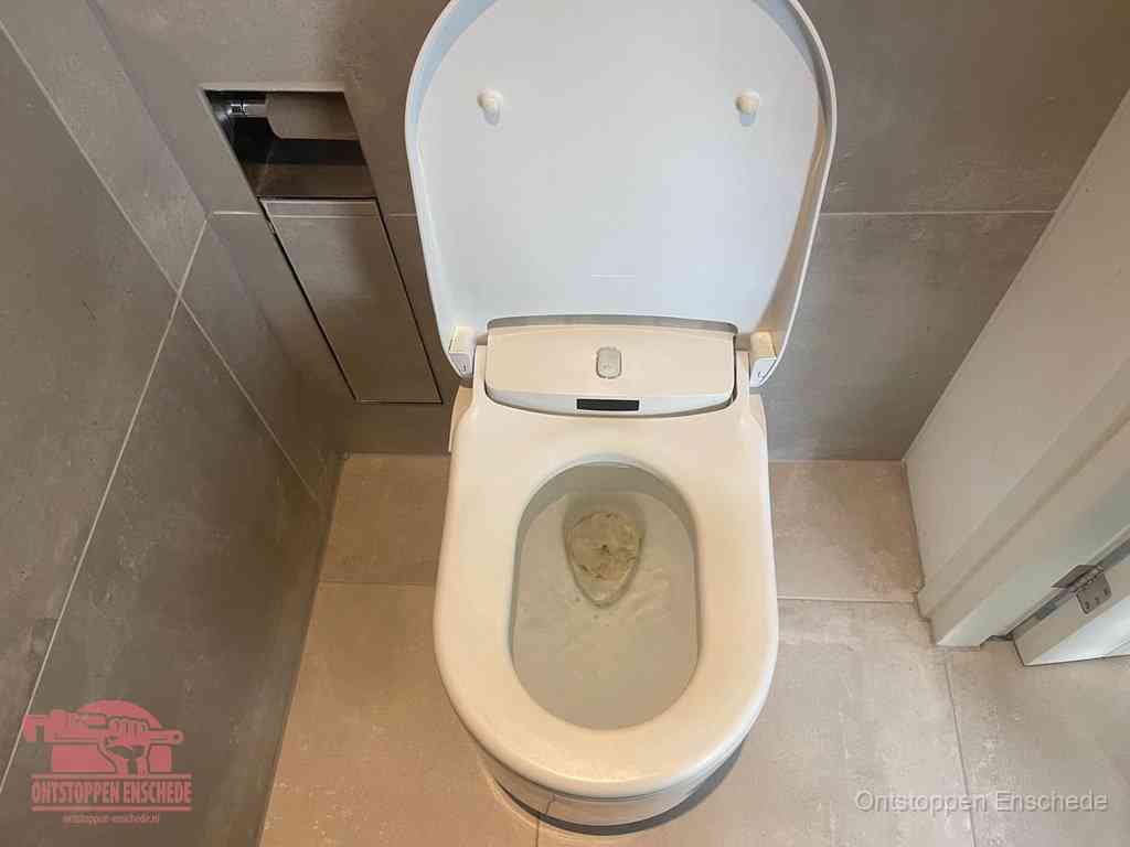 Een wit hangtoilet waarin een prop wc-papier op het water blijft drijven, een duidelijk signaal van een verstopte wc in Enschede