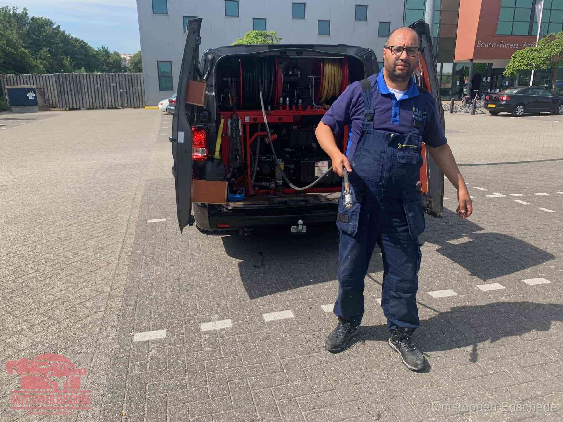Een monteur bij zijn bestelbus met een hogedruk- en rioolreinigingsunit, klaar om de oorzaak van terugkerende wc-verstoppingen aan te pakken in Enschede