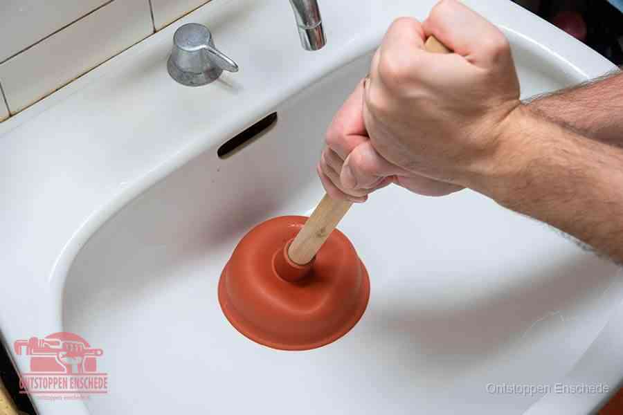 Twee handen gebruiken een rode rubberen plopper op een sanitair-afvoer om het toilet te ontstoppen in Enschede
