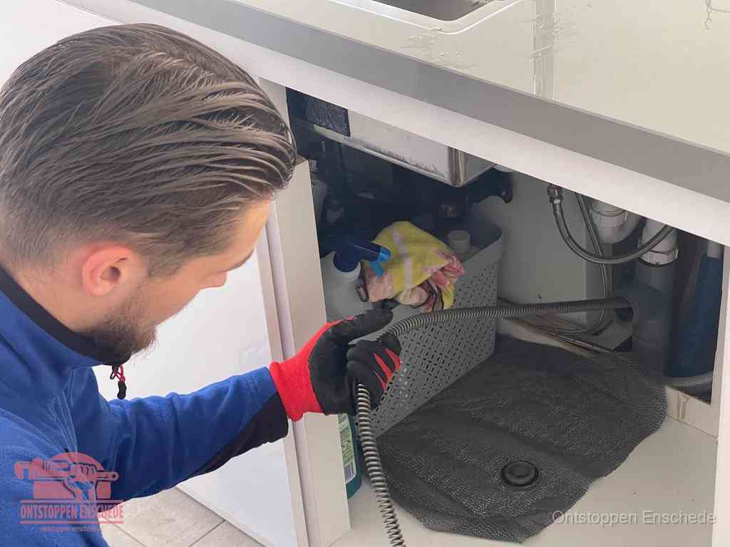 Een monteur voert een flexibele ontstoppingsveer in de afvoer om een verstopping voorbij de bocht van het toilet te bereiken in Enschede