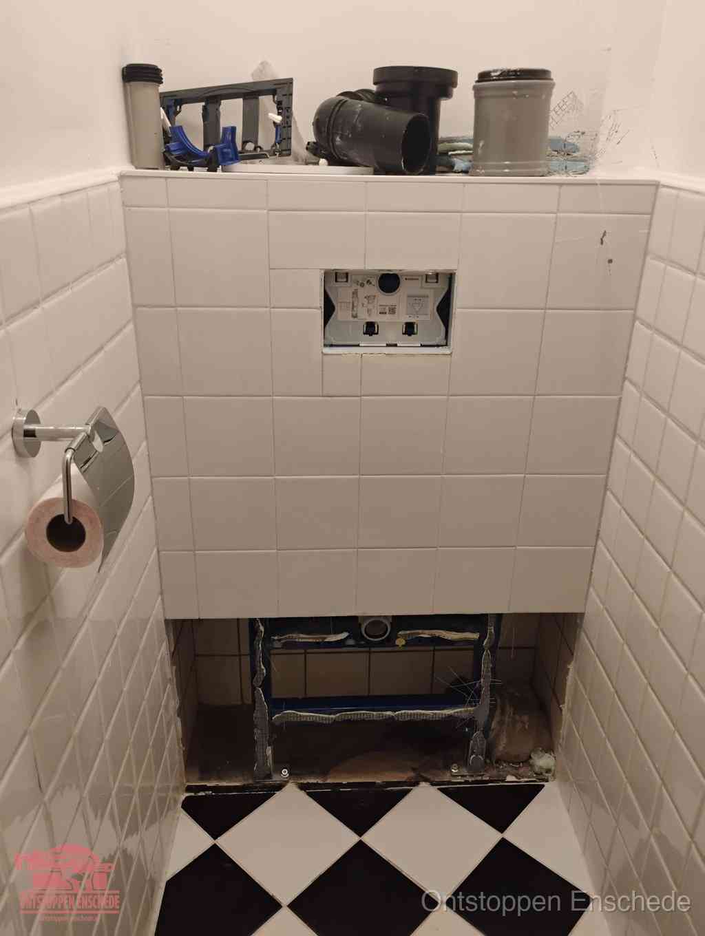 Een toiletruimte waar het hangtoilet en de inbouwreservoir-onderdelen zijn vrijgelegd voor onderhoud, periodiek nazicht voorkomt een wc-verstopping in Enschede