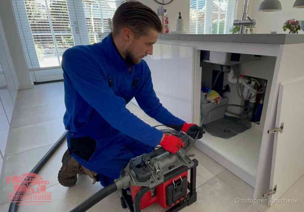 Een monteur voert een professionele elektrische ontstoppingsmachine in de afvoer onder de spoelbak tijdens het gootsteen ontstoppen in Enschede