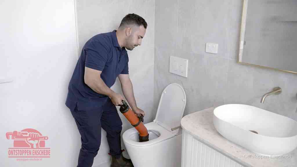Een man gebruikt een handmatige luchtdruk-ontstopper in een modern betegeld toilet om zelf de wc te ontstoppen in Enschede